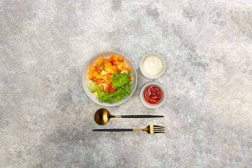 A flat lay of a bowl of tasty salad with sauces on the table