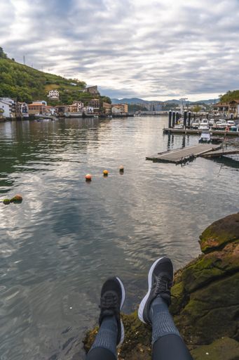 A vertical shot of a person wearing shoes with a view of a coastal town in Pasajes San Pedro, Gipuzkoa, Spain