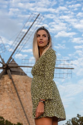 A vertical shot of a blonde Hispanic female in a flowered dress on the background of a windmill