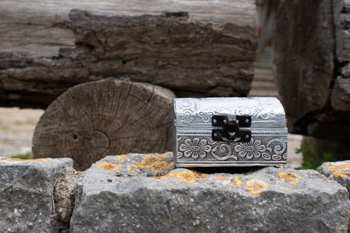 A closeup of a silver wooden jeweler box on a rough stone next to forest wooden ices in the forest