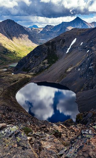 A vertical high angle shot of a lake near mountains under the cloudy skies