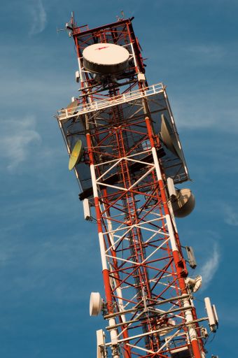 A vertical shot of a red and white communication tower against the blue sky