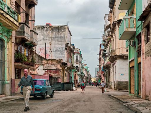 A wide shot of people walking in a narrow road near colorful old and new buildings in Havana, Cuba