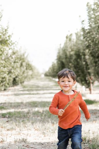 A cute smiling Caucasian kid running through Nevada orchard on the grass on a sunny day