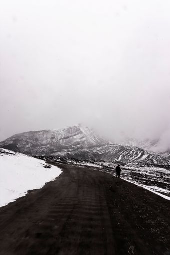 A view of an asphalt road going through mountains covered with snow against a cloudy sky