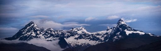A panoramic view of mountains peak covered with snow against blue cloudy sky
