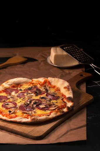 A fresh pizza with pepperoni and mushrooms on the chopping board, a piece of cheese and a grater