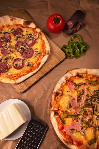 A fresh pizzas with pepperoni and mushrooms on the chopping board, a piece of cheese and a grater