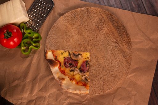A slice of mushroom pizza on a wooden tray, cheese, grater, tomato, and green peppers