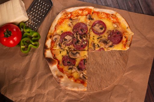 A three-quarter of mushroom pizza on a wooden tray, cheese, grater, tomato, and green peppers