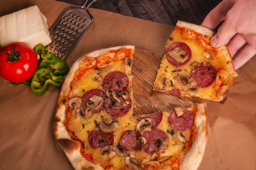 A mushroom pizza on a wooden tray, cheese, grater, tomato, and green peppers