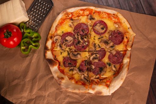 A fresh pizza with pepperoni and mushrooms on the chopping board, a piece of cheese and a grater