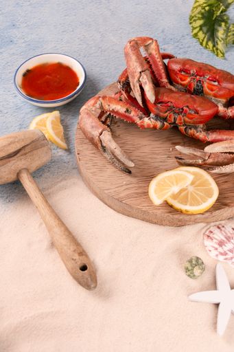 The freshly cooked crabs on a wooden tray served with red sauce and lemon slices