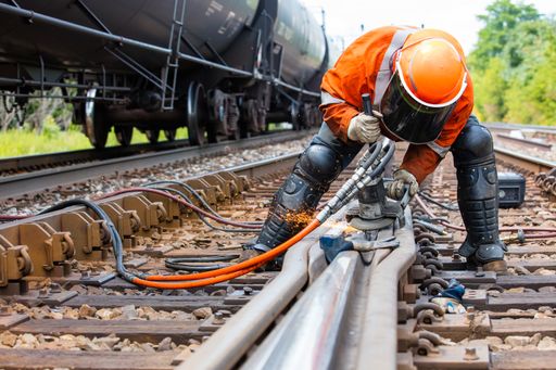 A worker in the process of a railroad track weld repair with a freight train passing