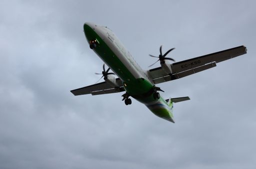 A low angle shot of a green and white plane under a blue cloudy sky