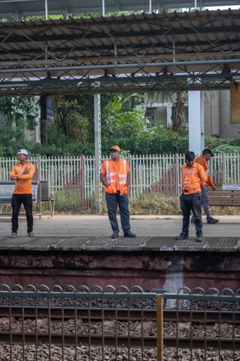 A vertical shot of three railway station workers in orange safety jackets and masks