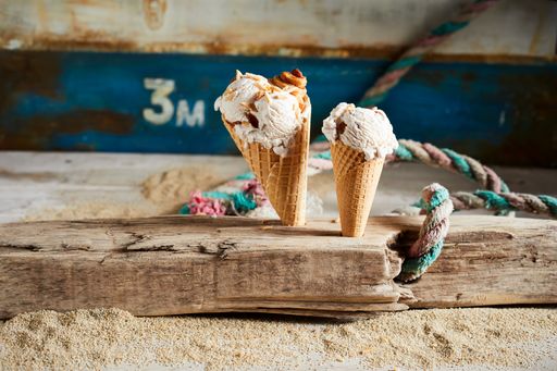 A closeup of two ice cream cones covered with caramel syrup on a wooden desk