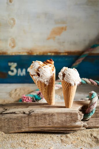 A vertical of two ice cream cones covered with caramel syrup on a wooden desk
