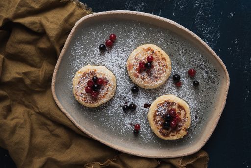 A top view of cottage cheese pancakes with wild berries and powdered sugar on a plate
