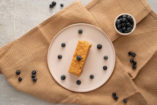 A slice of a cake topped with fresh blueberries on a white plate