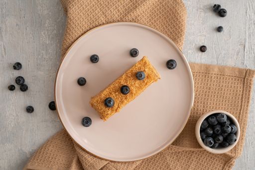 A slice of a cake topped with fresh blueberries on a white plate