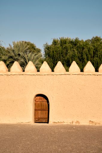 A vertical shot of a wooden entrance door to Al Jahili Fort in UAE under a blue sky on a sunny day