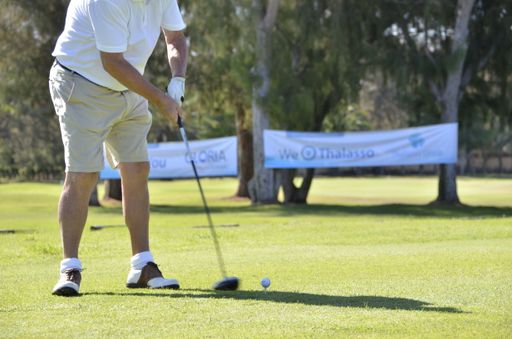 A shallow focus shot of legs of a man wearing shorts and playing golf in a field on a sunny day