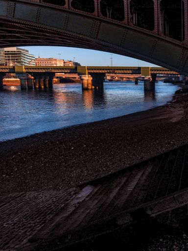 A vertical shot of the river under the metal bridges with the buildings in the background