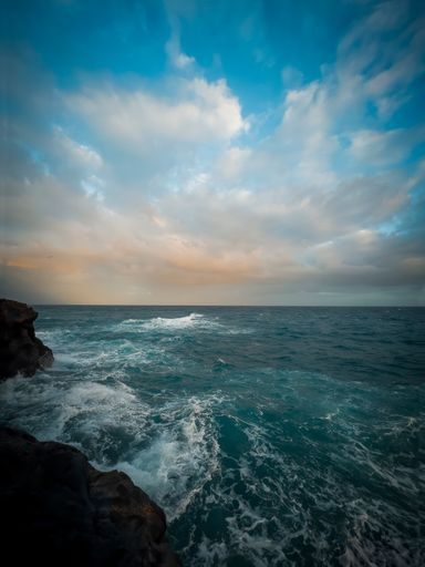 A vertical shot of the splashing sea water against a cloudy sky at sunset