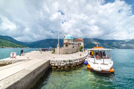 A landscape of a small church on Our Lady of the Rocks Island and a boat in the Bay of Kotor