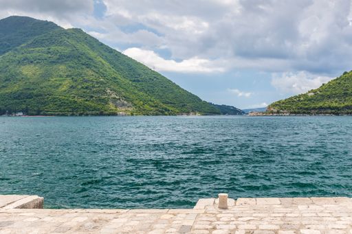 A panoramic view of the mountainous island of the Bay of Kotor from a pier on a cloudy day