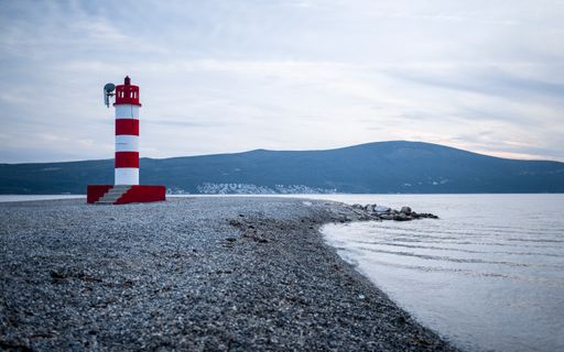 A striped red and white lighthouse standing on the shore of a sea on a cloudy day