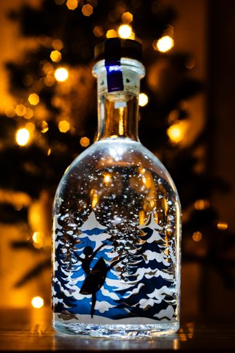 A vertical shot of ballerina dancing inside a snowy bottle with Christmas tree background