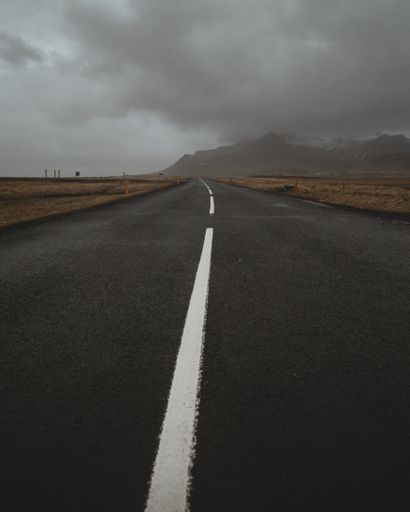 An empty concrete road with a white line in the middle under a gray cloudy sky
