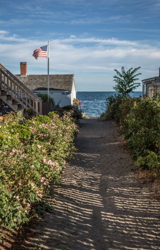 A vertical shot of the US flag next to the house with the sea in the background.