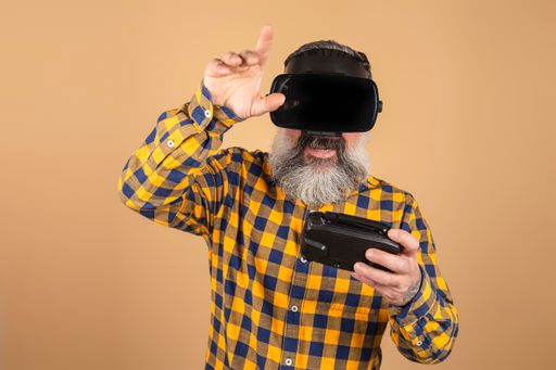 A cheerful Caucasian man with virtual reality glasses and a game controller wearing a plaid shirt
