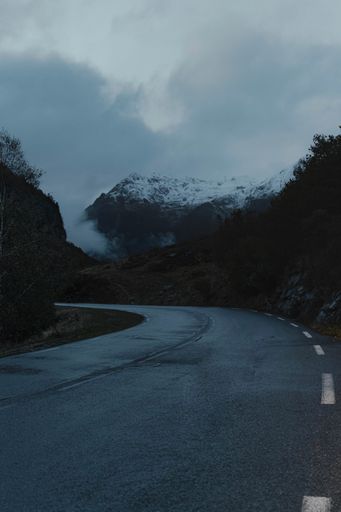 A vertical shot of an empty road passing through hills on a foggy day