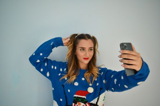 A closeup of a young Caucasian woman wearing a Christmas sweater and taking a picture on her phone