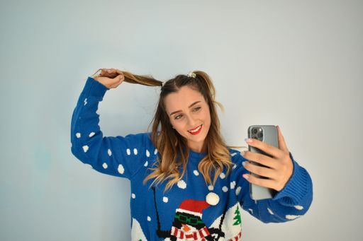 A closeup of a Caucasian woman smiling for a selfie while wearing a Christmas sweater
