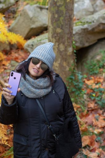portrait of a woman with sunglasses and wool hat taking self-portraits with smartphone in the forest on an autumn day in the morning. 