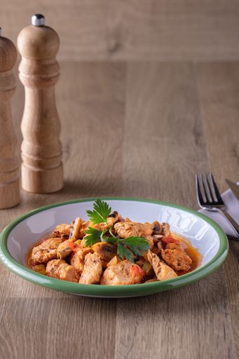 A vertical shot of a bowl of chicken and vegetable soup and some spices on a wooden surface