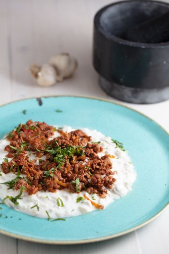 A vertical high angle shot of a plate of cream and meat with some garlic on a wooden surface