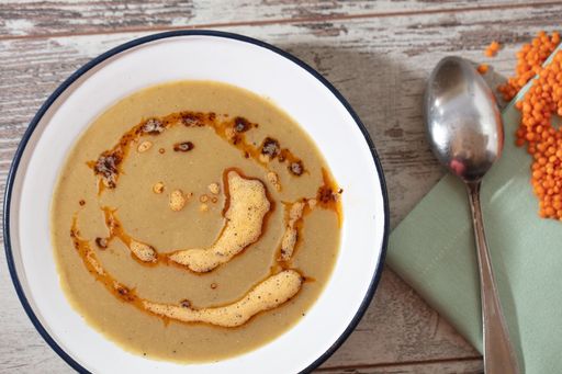A high angle shot of a white bowl of soup and a spoon on a wooden table