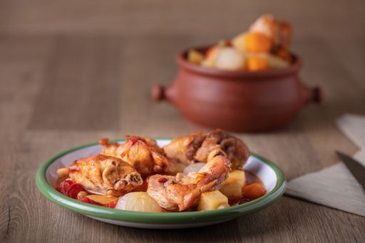 A high angle shot of a pot and a plate of chicken and vegetables on a wooden surface