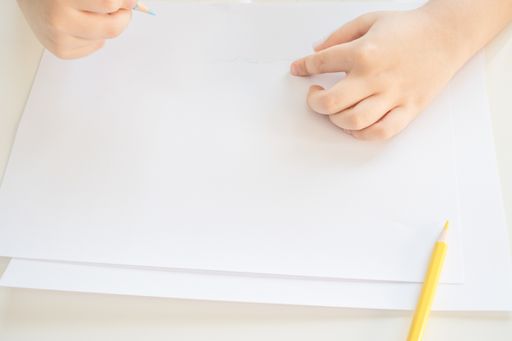 A high angle shot of a child drawing with blue and yellow pencils on a white paper