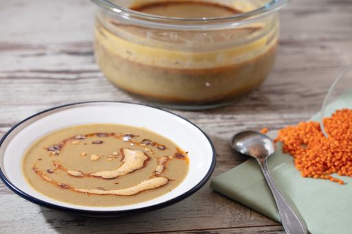 A high angle shot of a pot and a bowl of soup and a spoon on a wooden surface