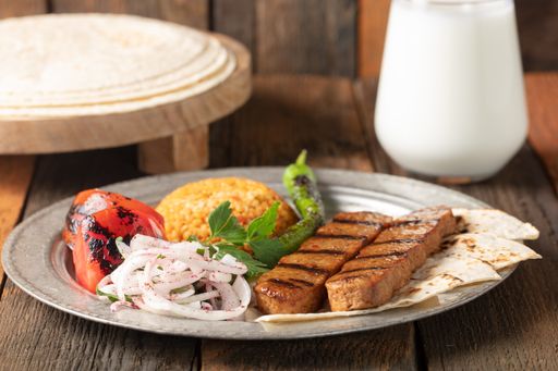 A high angle shot of a plate of kebab, vegetables, and spicy rice on a wooden surface