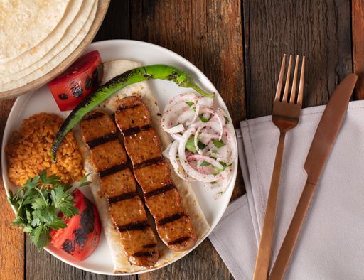 A high angle shot of a plate of kebab, grilled pepper and tomatoes on a wooden surface