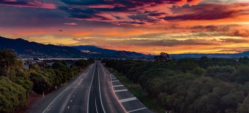 A scenic view of an empty road through the forests with the background of mountains in the sunset under cloudy sky