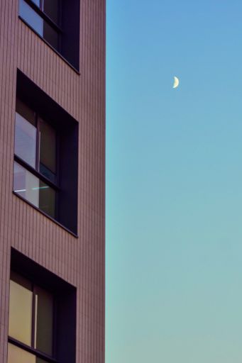A vertical shot of a small shining moon near a building facade
